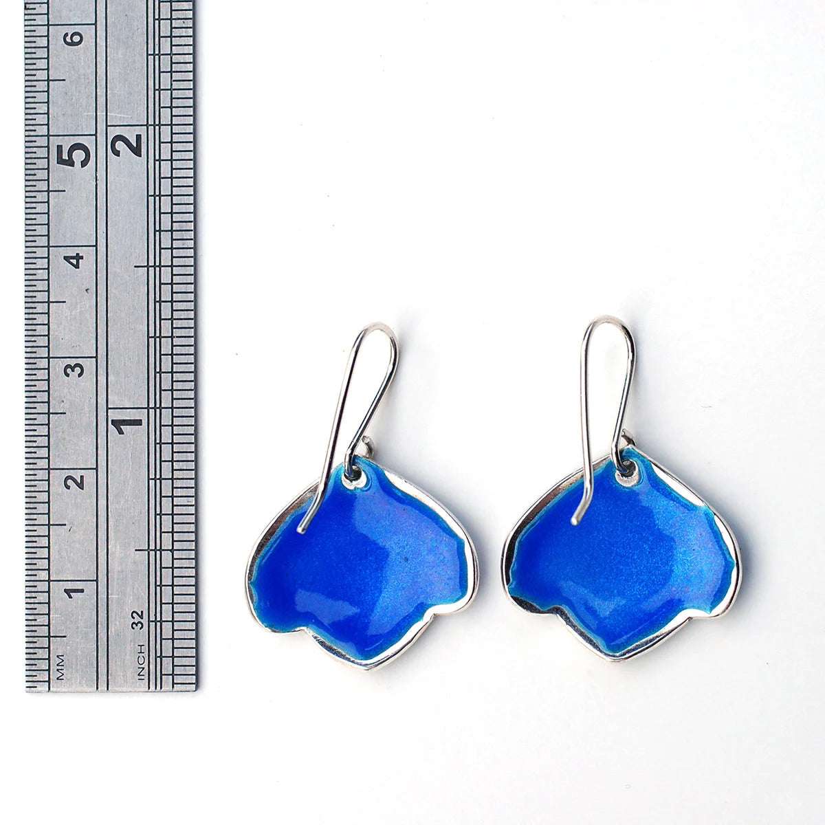 Blue leaf enamel earrings on a white background with a ruler, back view.
