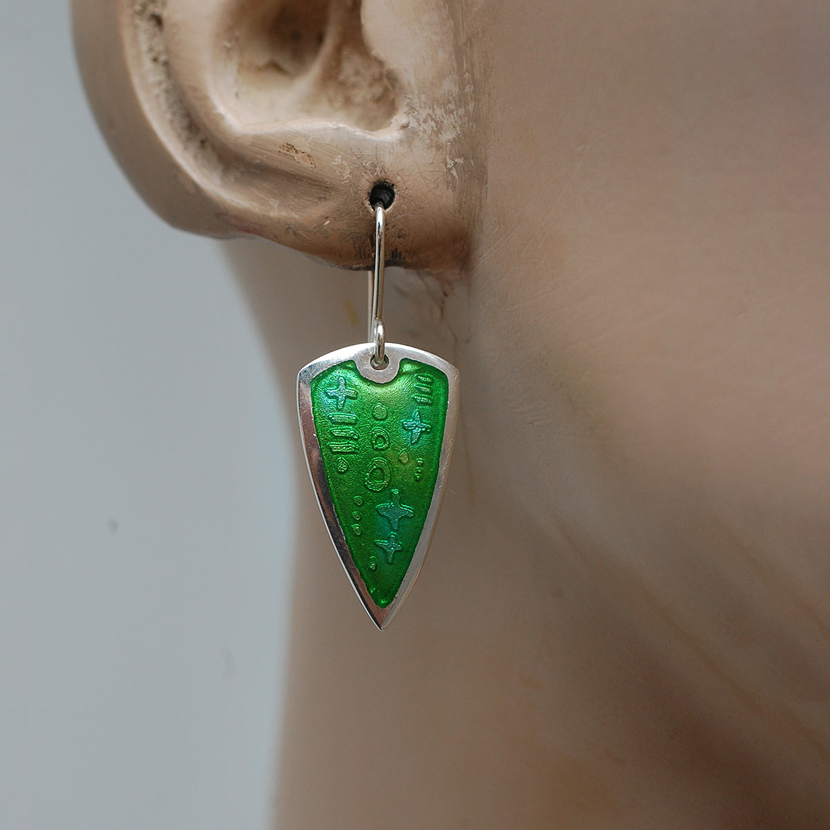 Silver earrings with green enamel over an etched pattern on a mannequin