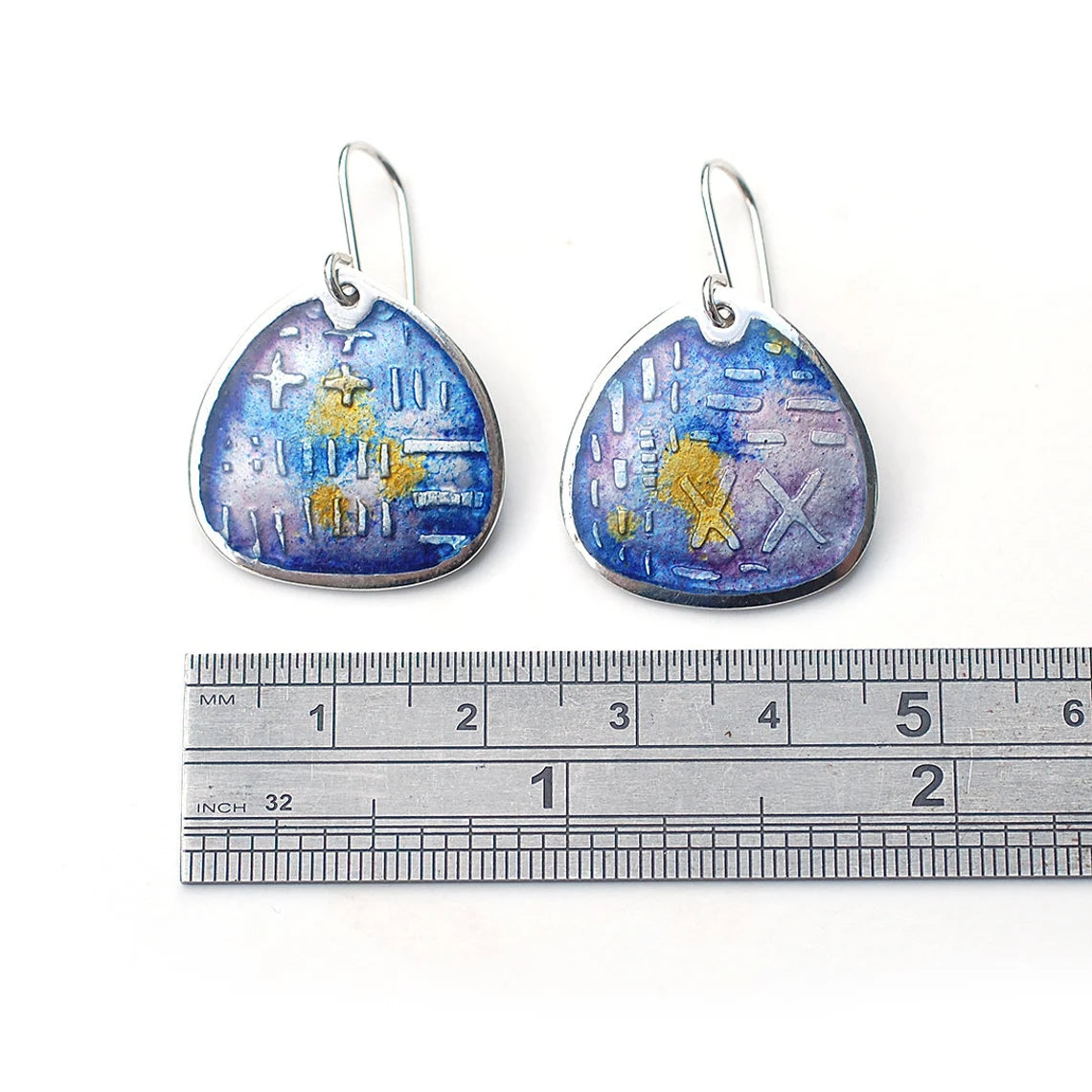Fat teardrop shaped enamel earrings, etched silver, shades of purple and yellow. On a white background with a ruler.
