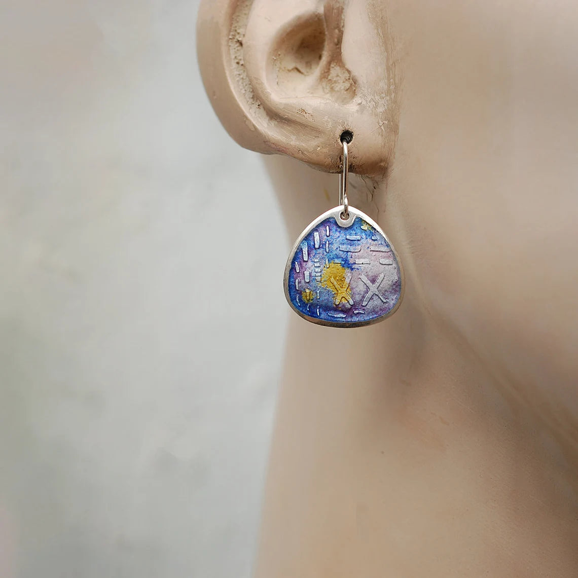 Fat teardrop shaped enamel earrings, etched silver, shades of purple and yellow. On a mannequin.