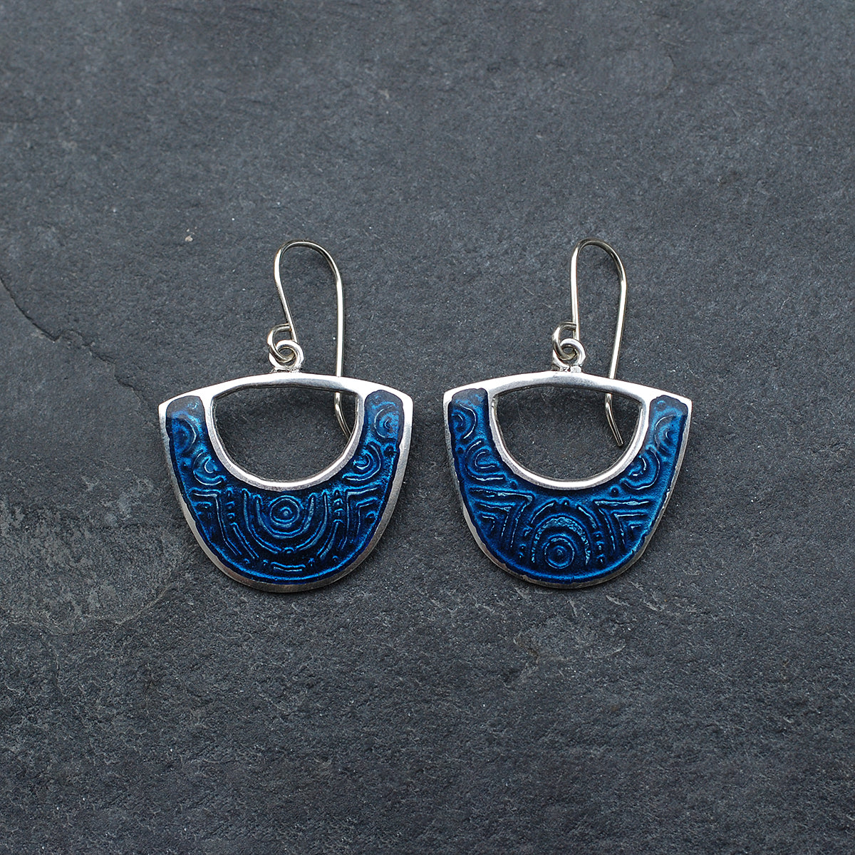 Midnight blue enamel on silver earrings, shield cutout shape, on a  slate grey background