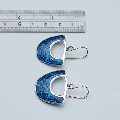 Midnight blue enamel on silver earrings, shield cutout shape, on a white background, with ruler, side view