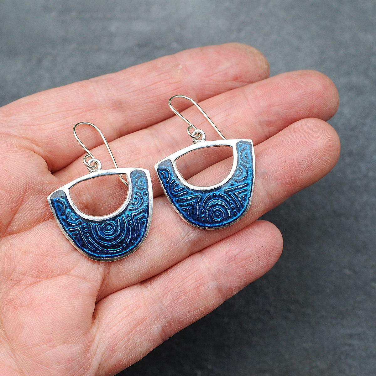 Midnight blue enamel on silver earrings, shield cutout shape, on a hand