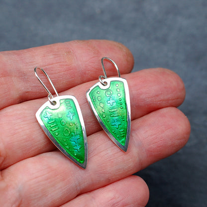 Silver earrings with green enamel over an etched pattern on a hand