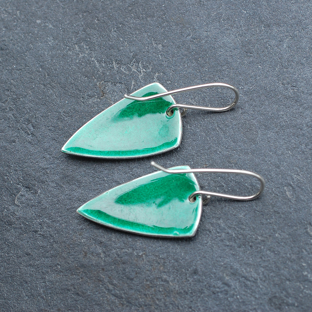 Silver earrings with green enamel over an etched pattern on a slate grey background, back view
