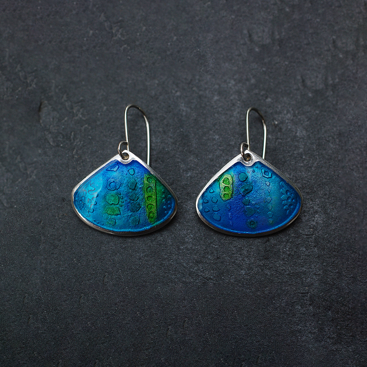 Onion shaped etched silver and enamel earrings in blues and greens, on a slate grey background