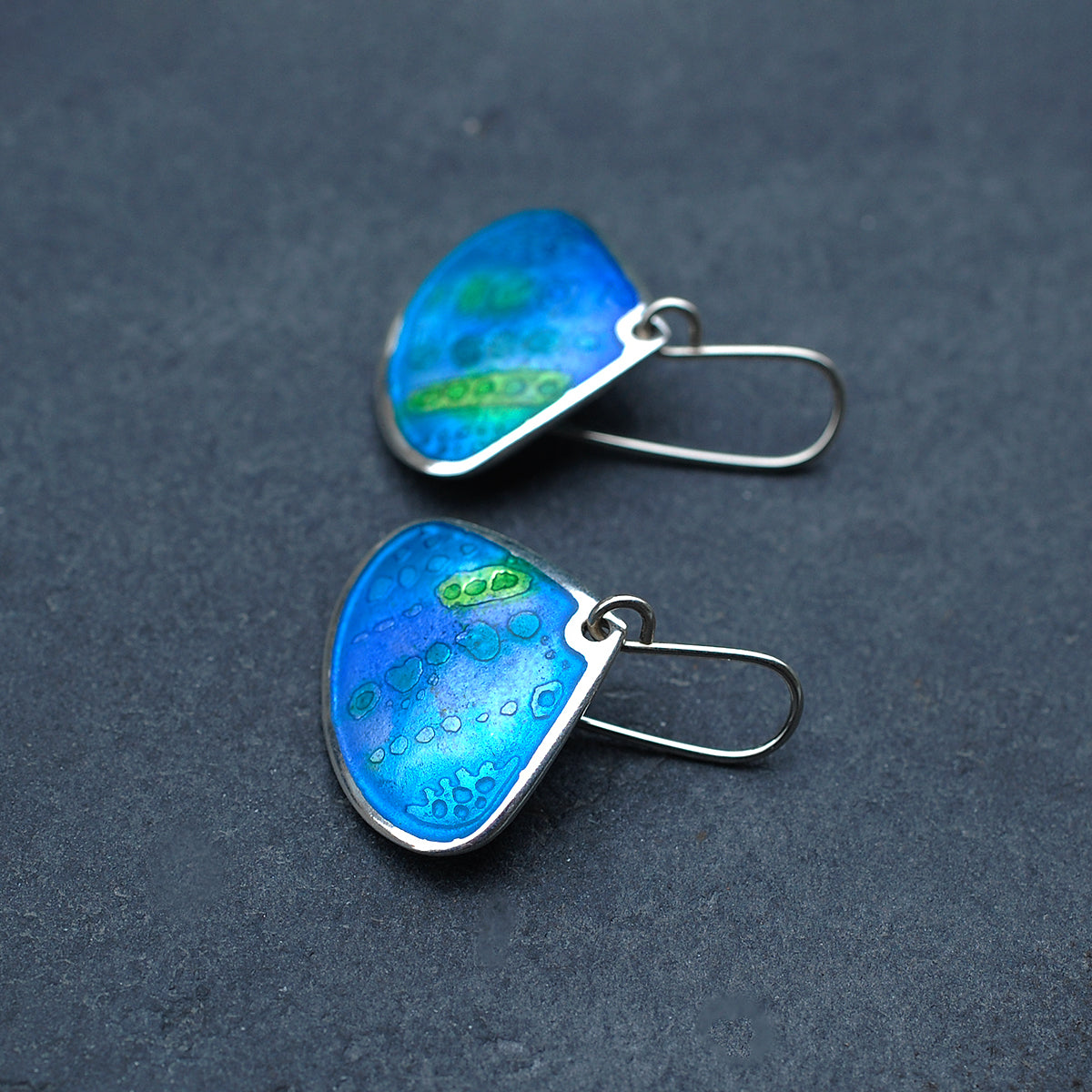 Onion shaped etched silver and enamel earrings in blues and greens, on a slate grey background, side view