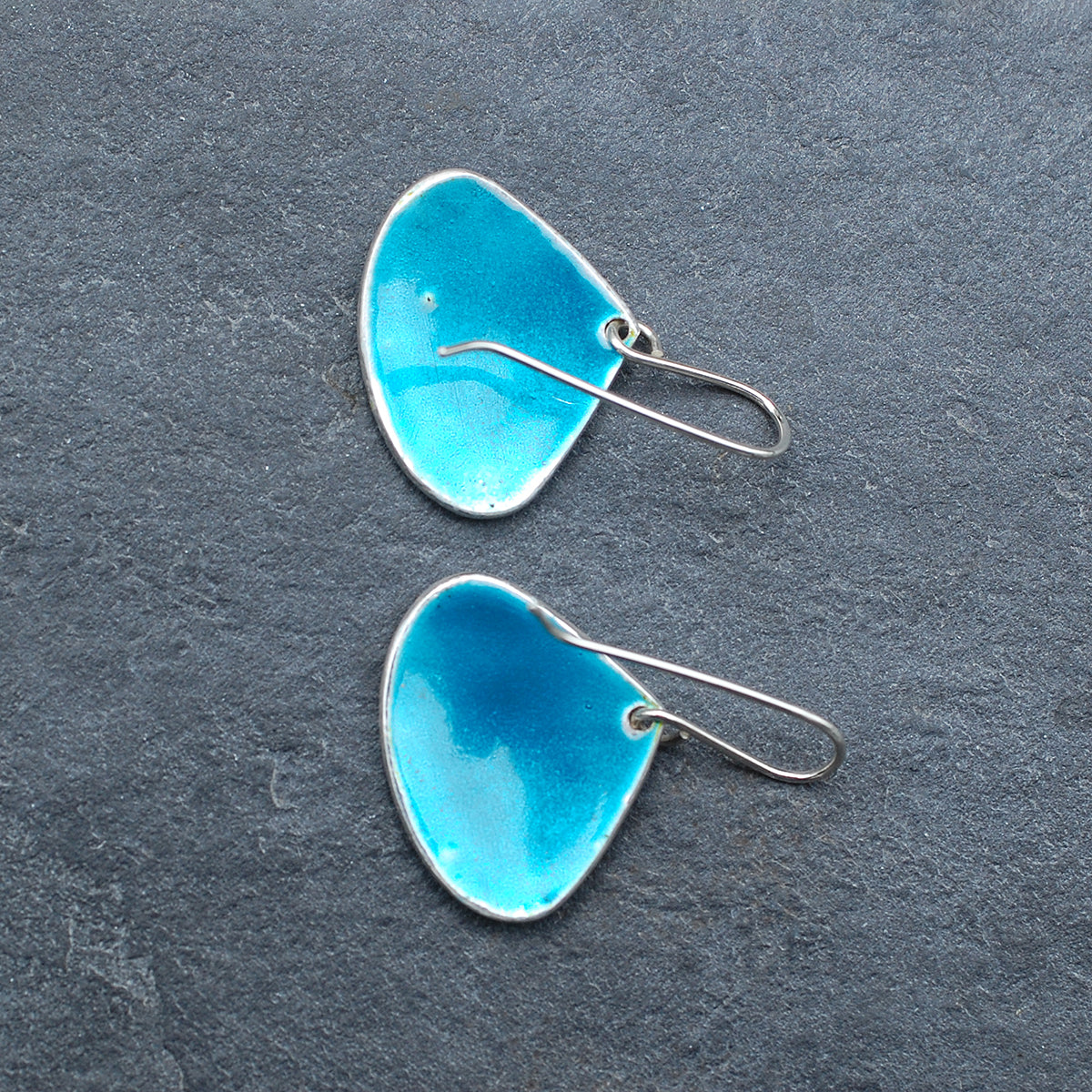 Onion shaped etched silver and enamel earrings in blues and greens, on a slate grey background, back view
