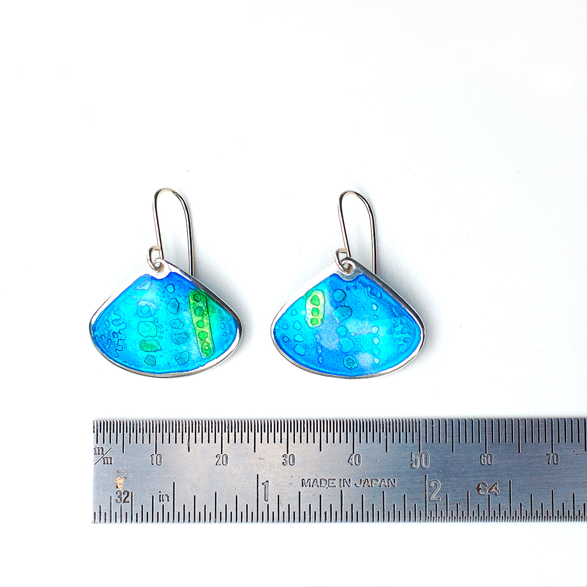 Onion shaped etched silver and enamel earrings in blues and greens, on a white background with ruler