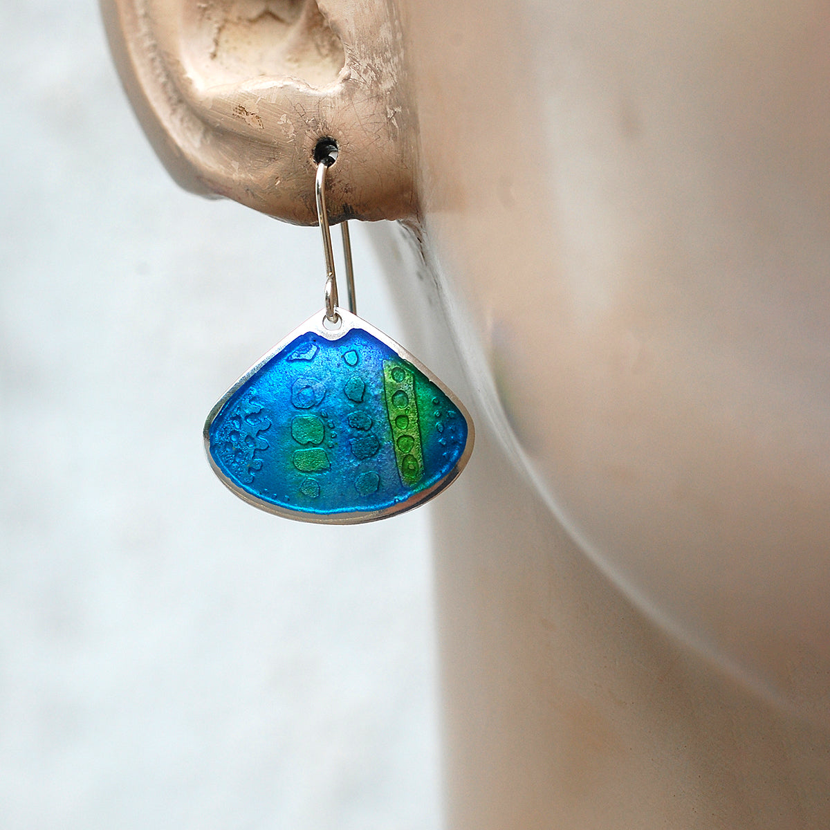 Onion shaped etched silver and enamel earrings in blues and greens, on a mannequin