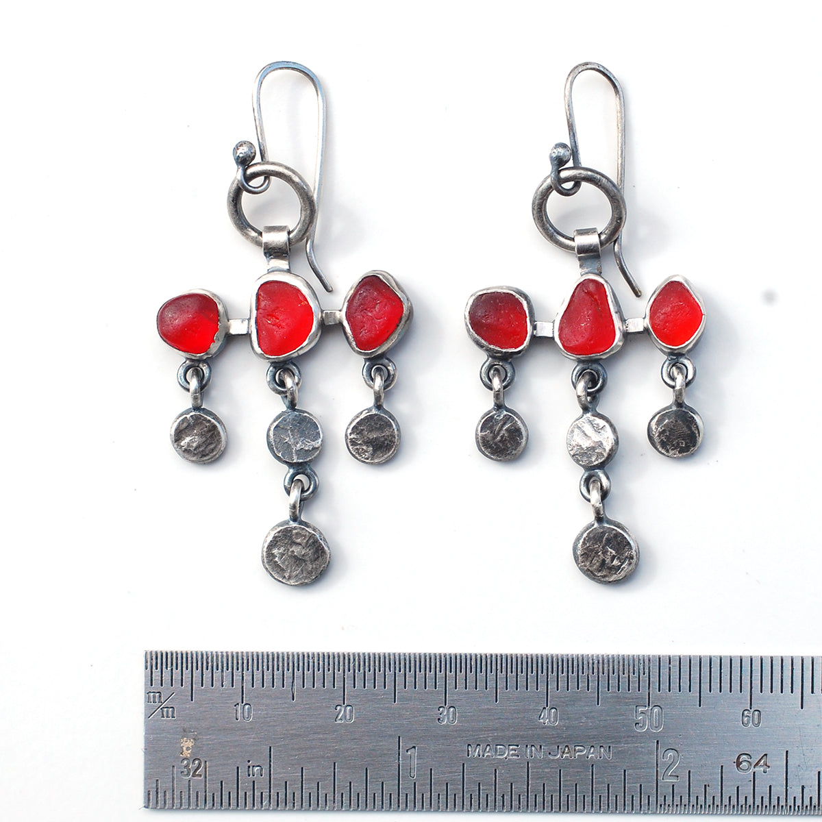 
Dot and dangle red sea glass earrings on a white background with ruler.
