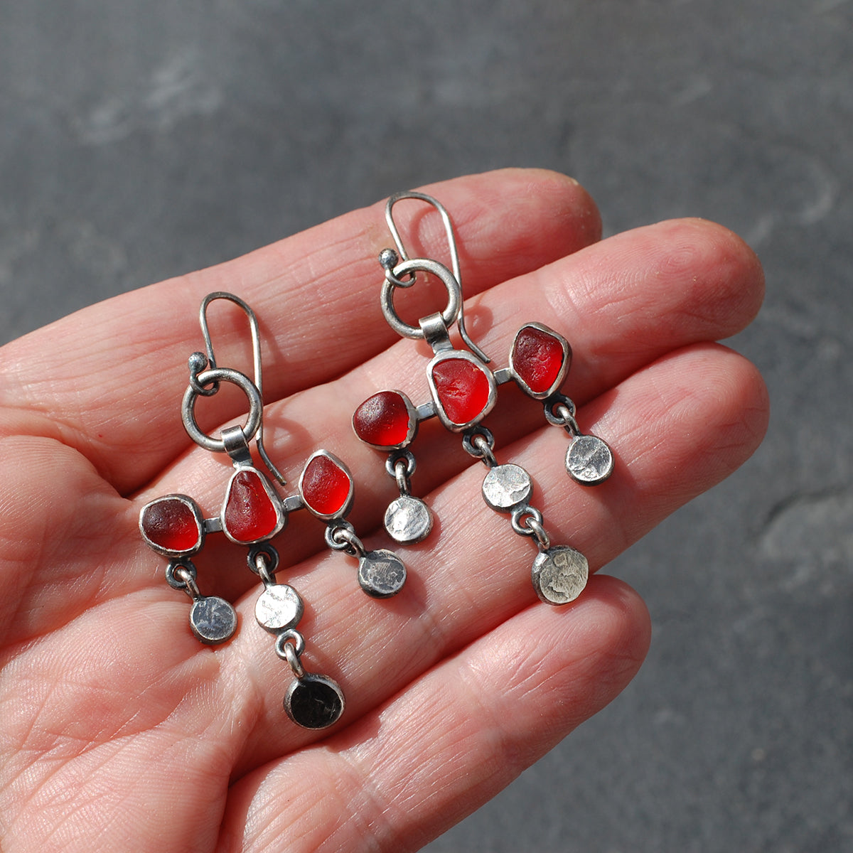 
Dot and dangle red sea glass earrings on a hand.
