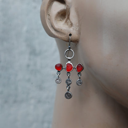 
Dot and dangle red sea glass earrings on a mannequin.
